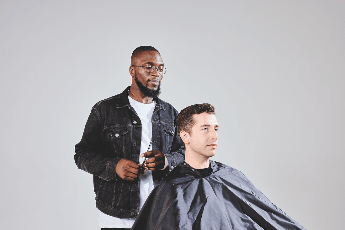 A barber tending to a client in a chair covered in a black smock.